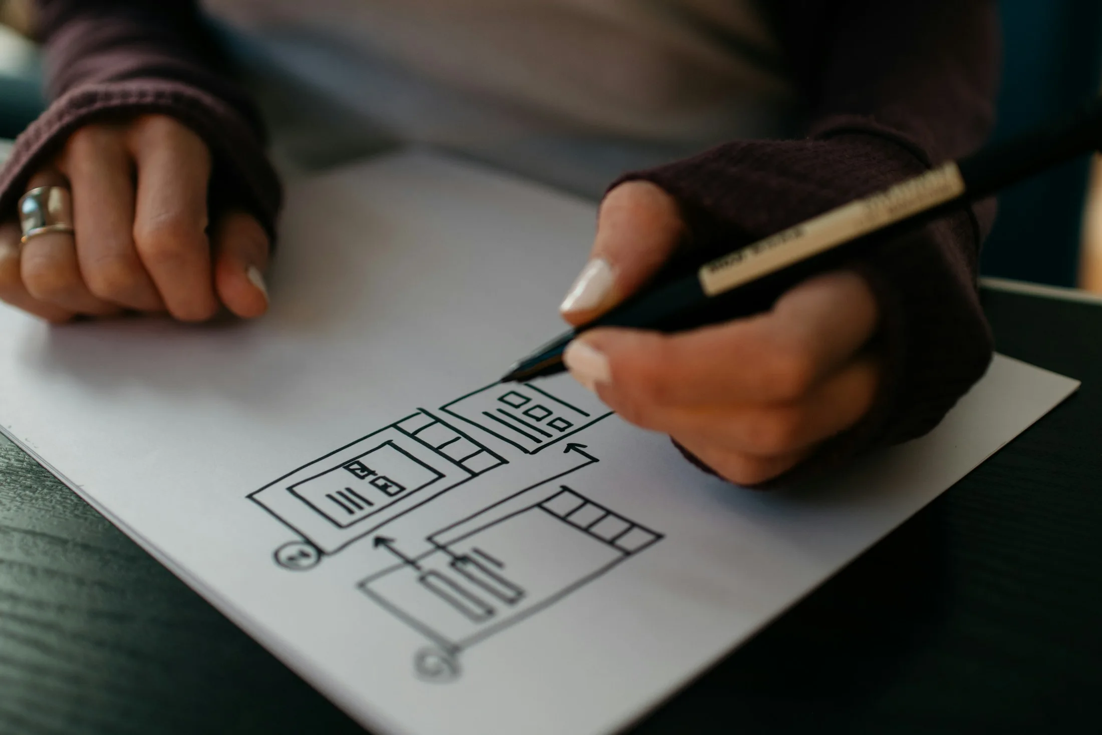 A hand drawing interface layouts and user flows on paper