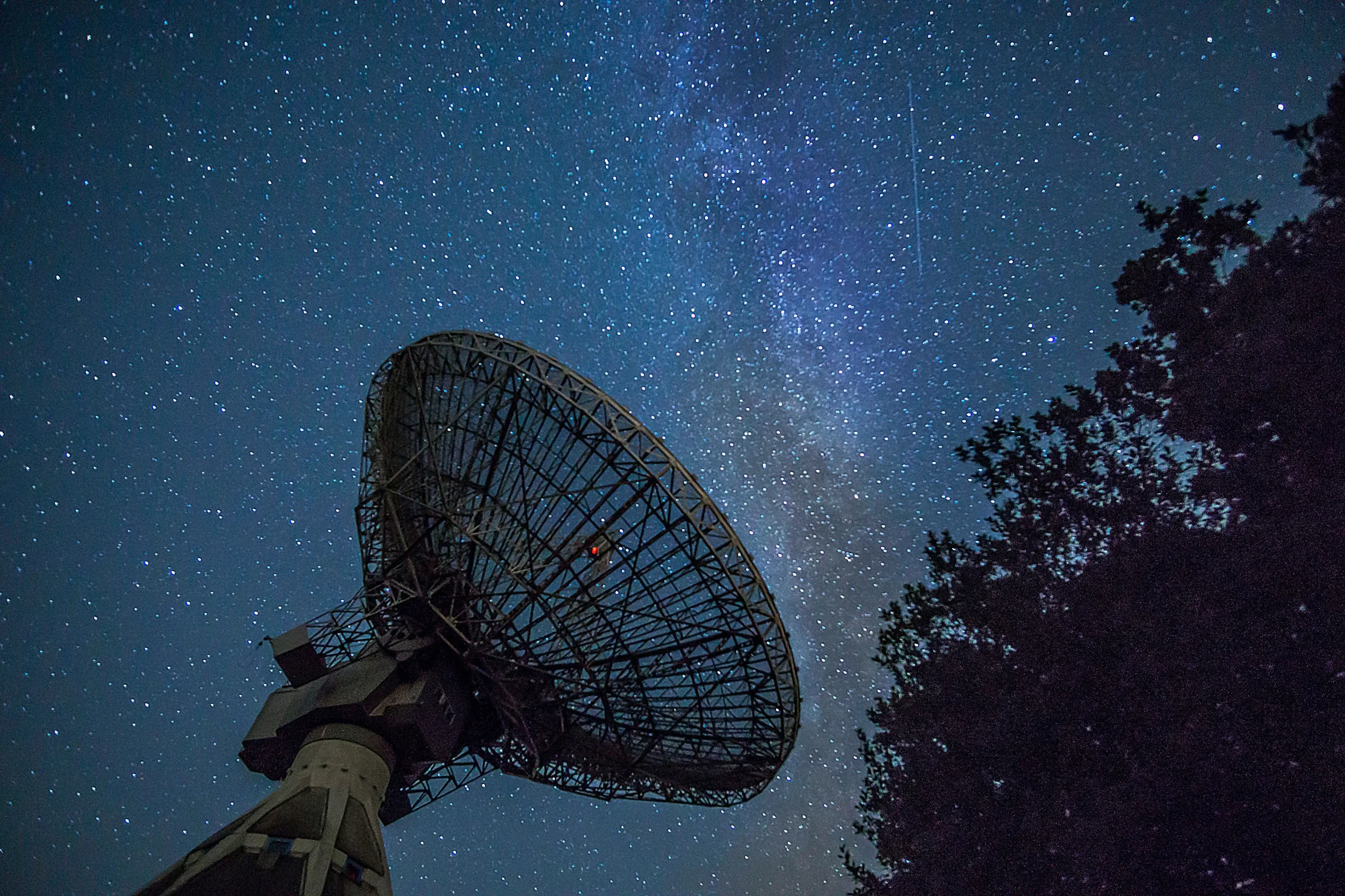 A giant radio telescope reaching toward a star-filled night sky